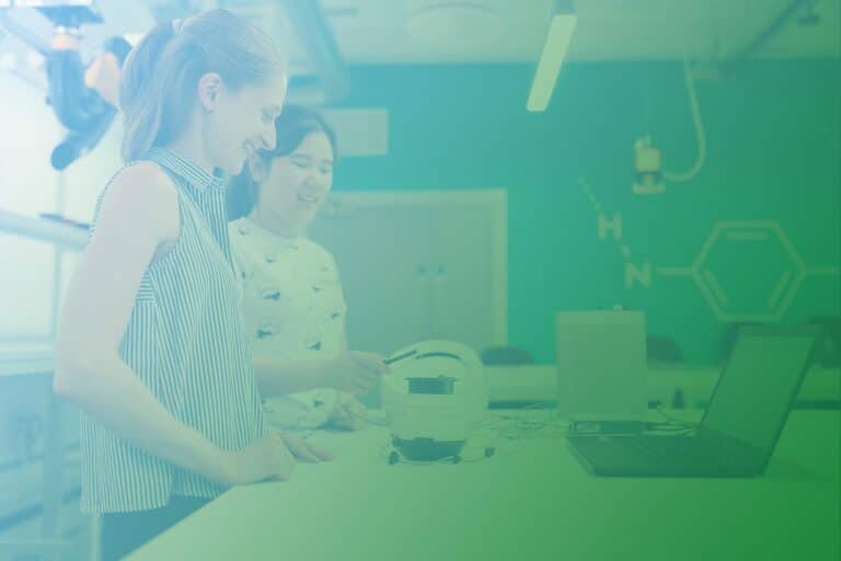 Produktdigitalisierung ist in Zeiten des Internet der Dinge in vielen Unternehmen notwendig: Zwei Frauen stehen an einem Tisch mit Laptop und Gerät